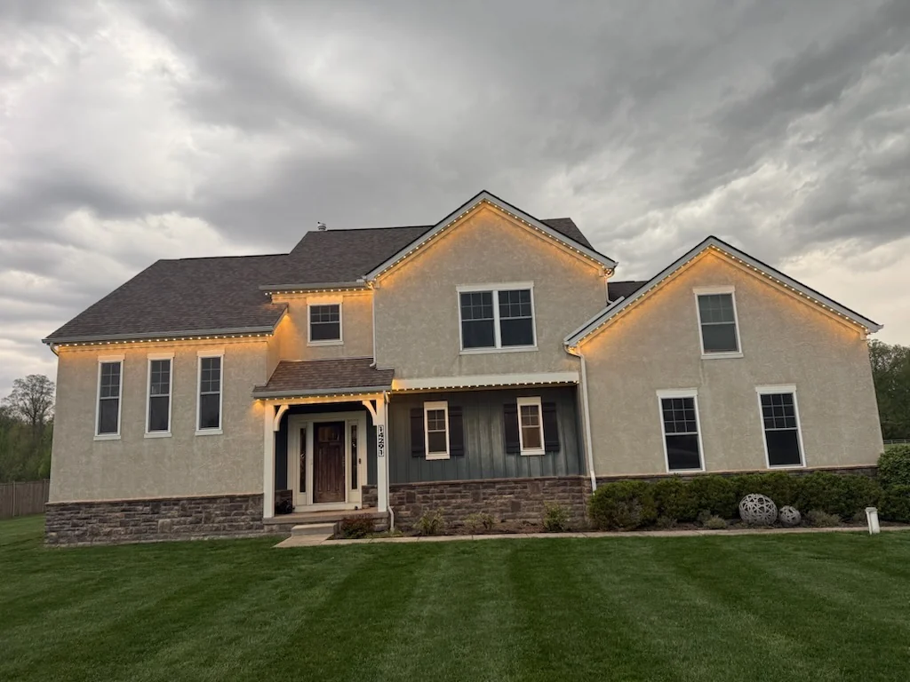 190 ft Dublin OH stucco estate front view at twilight with warm white permanent Christmas lights tracing the roofline and peaks
