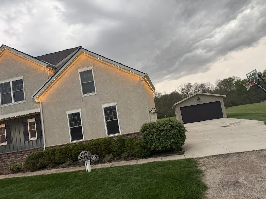 190 ft Dublin OH stucco estate side view with detached garage, warm white permanent Christmas lights along the soffit