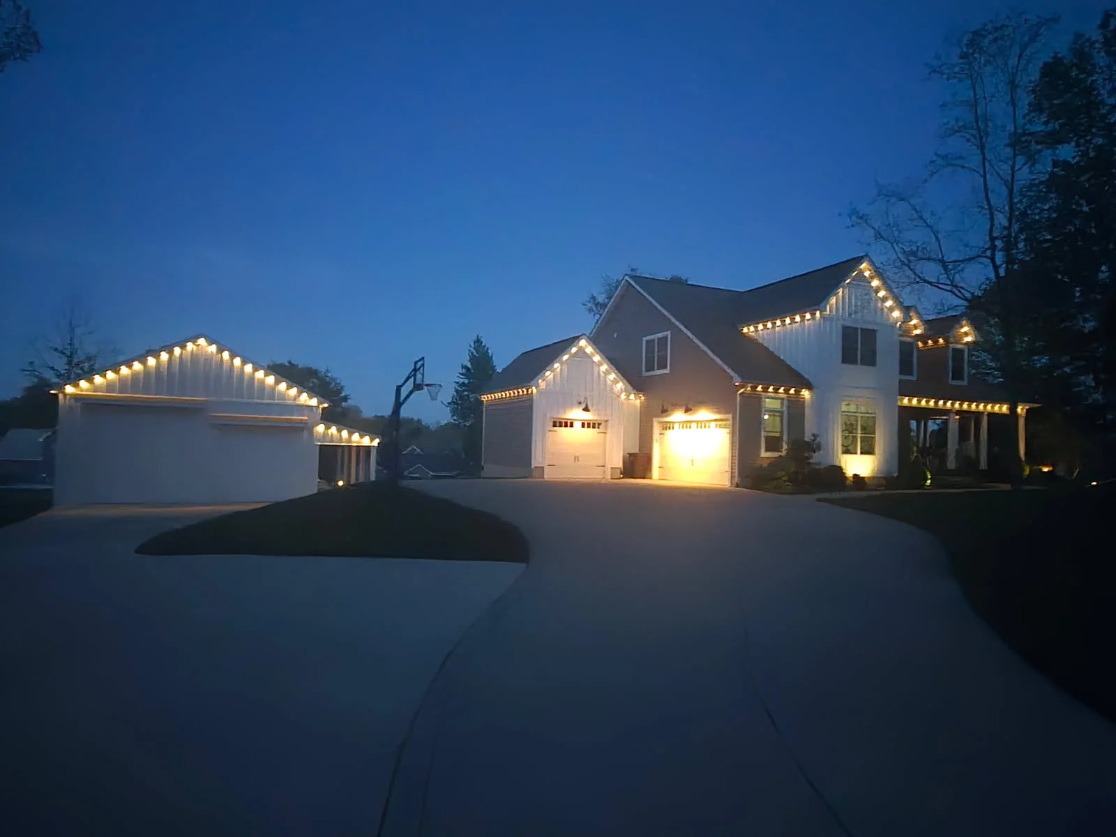 333 ft Columbus farmhouse with detached garage and main house lit by Govee permanent lights, three garage bays glowing warm