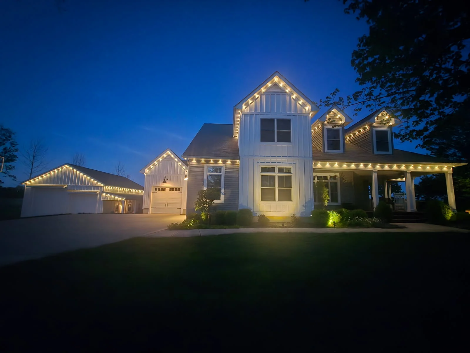 333 ft Columbus farmhouse front view at twilight, detached garage on the left, main house with multiple peaks all lit by Govee permanent lights