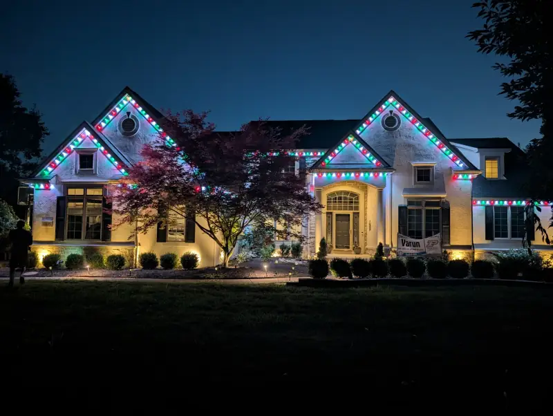 Red and green permanent Christmas lights on large estate home at night